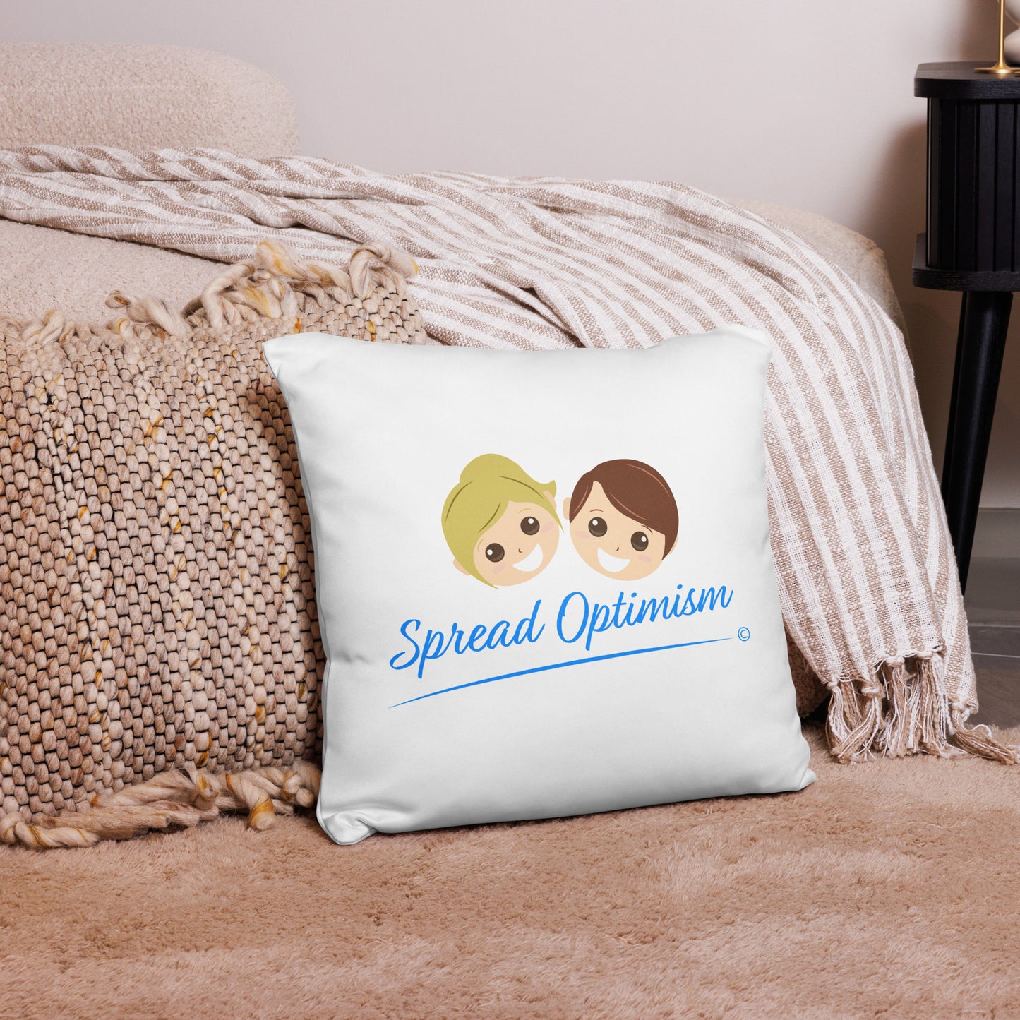 Radiant 18x18 throw pillow spreading positivity with the uplifting message 'Spread Optimism,' placed on a pink carpet with a coordinating rug and a charming pink checkered scarf.