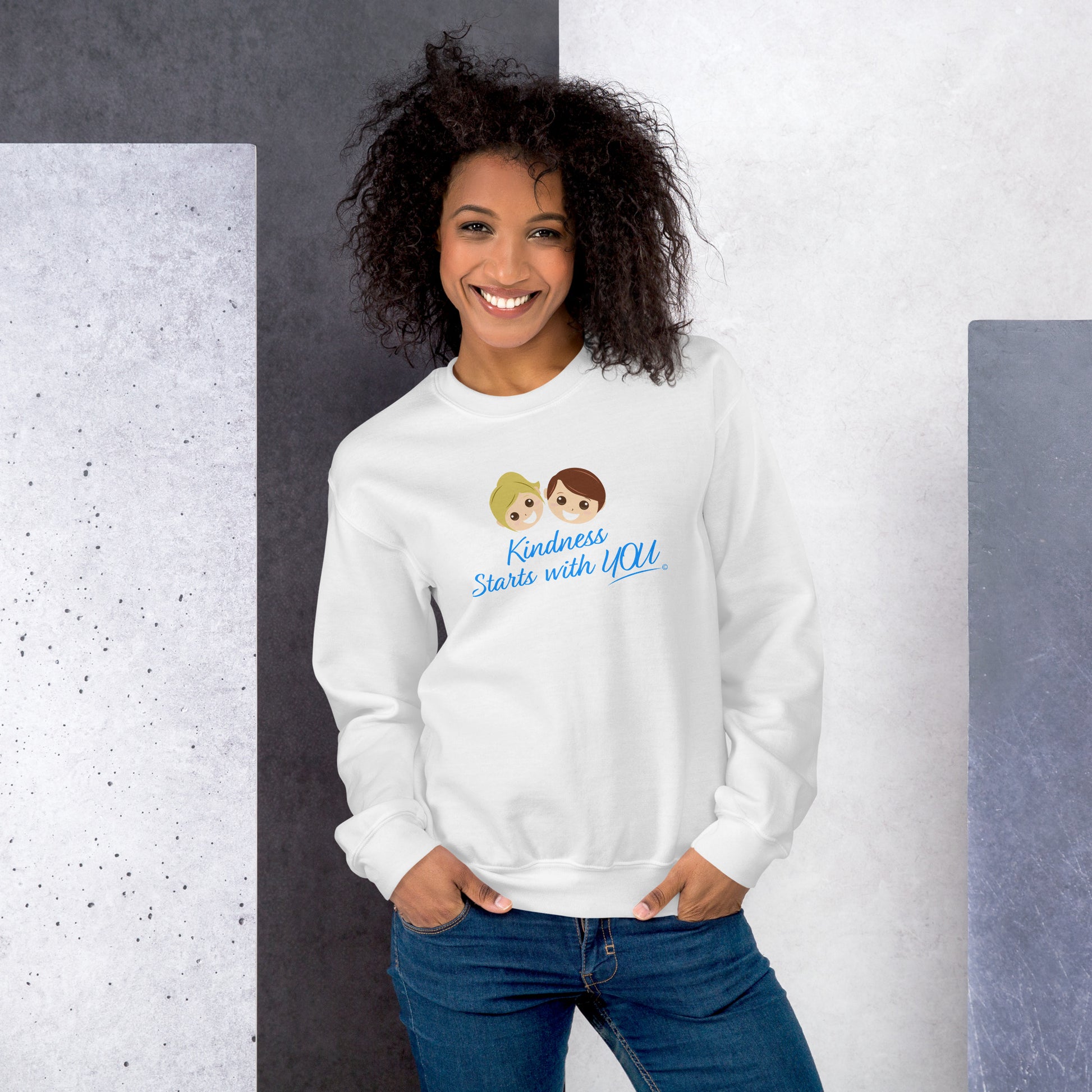 A smiling woman modeling a cozy unisex sweatshirt in white, featuring the uplifting quote 'Kindness Starts with You' in bold lettering.
